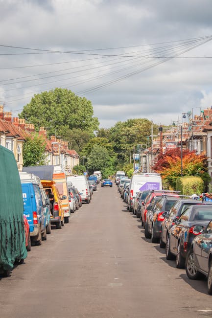 A straight residential street in Finchley lined with parked cars on both sides, including sedans, vans, and small trucks. The pavement is clear, with a variety of houses featuring brick façades and t